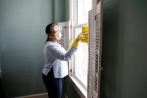 A woman in white shirt cleaning window with yellow gloves.