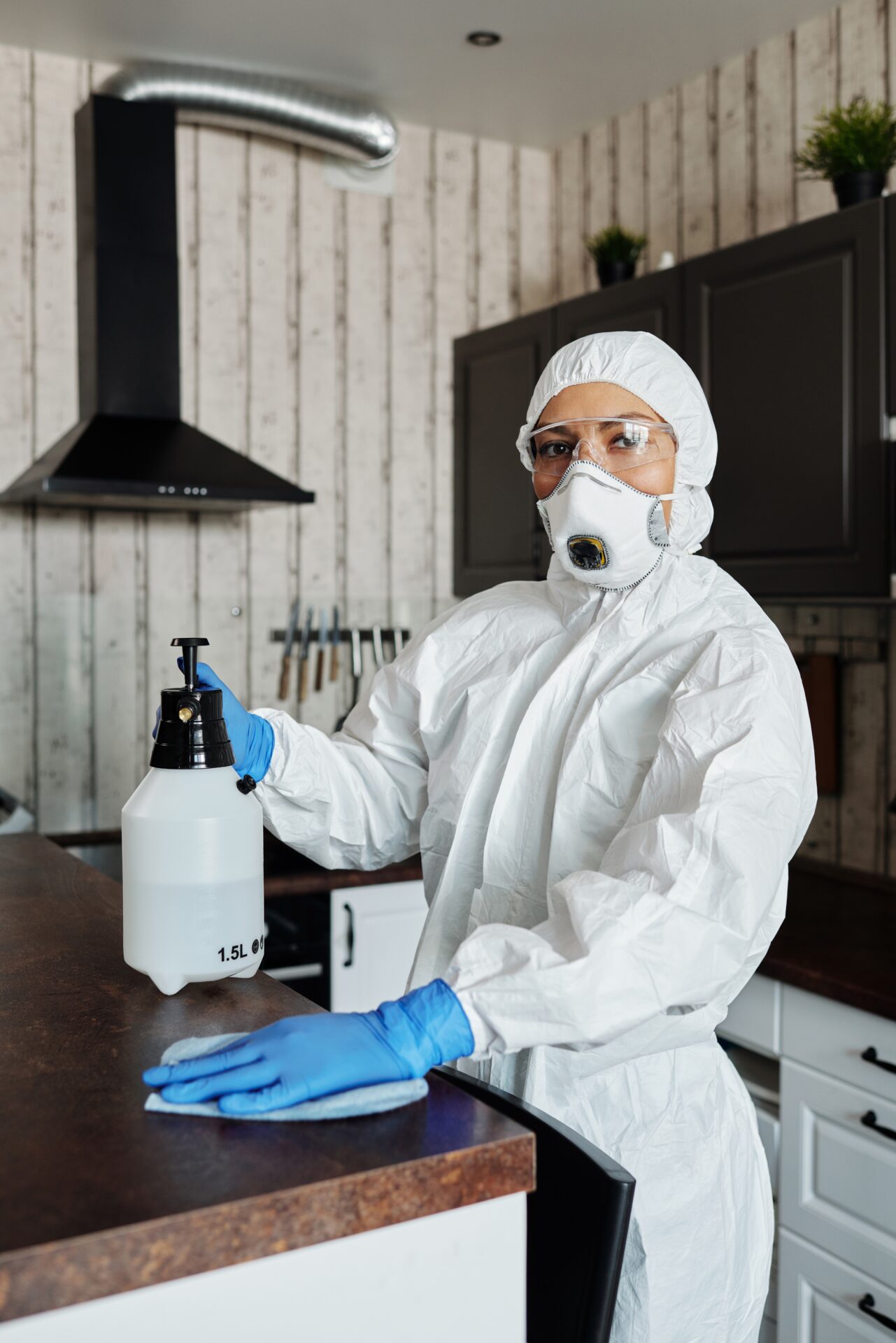 A person in white suit and mask holding a spray bottle.